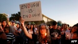 Varios dolientes se ponen de pie durante una vigilia con velas por las víctimas del tiroteo de Marjory Stoneman Douglas High School en Parkland, Florida.