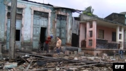 Dos hombres limpian escombros en una casa que fue parcialmente destruida por el paso del huracán Sandy.