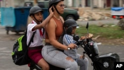 Una mujer transporta a dos niños en una motocicleta eléctrica por las calles de La Habana Vieja, el 24 de noviembre de 2023. Conseguir uniformes, zapatos adecuados, merienda escolar y otros artículos básicos es un reto enorme para los padres cubanos. (AP/Ismael Francisco)