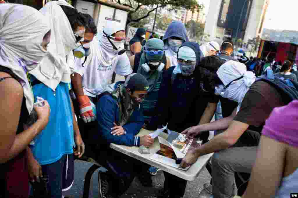 Un grupo de personas que se cubren el rostro permanecen en protestas opositoras